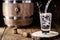 Pouring distilled alcohol into a shot glass, drops flying, served on wooden planks. Vintage bench with oak barrel and wooden