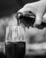 POURING A FIZZY COLA DRINK FROM A GLASS BOTTLE INTO A TALL GLASS