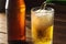 Pouring foaming beer into glass mug with drops near cold beer bootle on wooden table, craft brewing