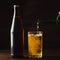 Pouring foaming beer into glass mug with drops near cold beer bootle on wooden table, craft brewing concept