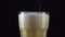 Pouring fresh and cold craft beer into a glass with white foam on top on black background. Flowing foamy wheat or lager beer on