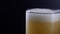 Pouring fresh and cold craft beer into a glass with white foam on top on black background. Flowing foamy wheat or lager beer on