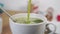 Pouring fresh green matcha tea with froth into a white teacup on the kitchen table