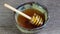 Pouring golden sweet honey on green bowl ceramic with a wooden honey dipper on wood table.