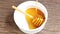 Pouring golden sweet honey on white bowl ceramic with a wooden honey dipper on wood table.