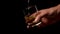 Pouring golden whiskey into a glass with ice cubes. Holding in hand on a black background.