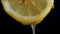 Pouring honey on fresh slice lemon against black background