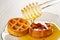 Pouring honey with honey dipper on round waffle in saucer on wooden table