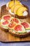 Pouring honey on toasts with cream cheese topped with fresh ripe figs and peaches. Wholegrain rye bran bread on wood cutting board