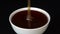 Pouring honey in white bowl. Closeup honey dripping in black background, macro