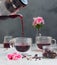 Pouring hot hibiscus tea into glass cup and pink flowers on light grey stone background. Making hibiscus tea. Hot drink