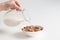 Pouring milk into the bowl with multigrain natural flakes on a white background. Healthy food.