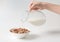 Pouring milk into the bowl with multigrain natural flakes on a white background. Healthy food.