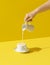 Pouring milk in a cup, on yellow background. Milk overflow from a cup