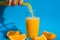 Pouring orange juice stream from jug into glass of squeezing Orange juice with sliced fruits on blue background. Fruit