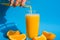 Pouring orange juice stream from jug into glass of squeezing Orange juice with sliced fruits on blue background. Fruit