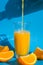Pouring orange juice stream from jug into glass of squeezing Orange juice with sliced fruits on blue background. Fruit