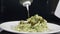 Pouring pesto sauce into plate with cooked pasta on black background. Slow motion. Cooking delicious meal. Italian