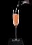 Pouring pink rose champagne from bottle to glass on black marble board on black background. Space for text