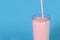 Pouring pink strawberry milkshake or cocktail into glass over blue background