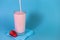 Pouring pink strawberry milkshake or cocktail into glass over blue background