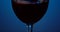 Pouring Red wine forms beautiful wave. Wine pouring in wine glass over blue background. Close-up shot. Low key