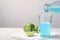 Pouring refreshing light blue drink into glass on white table, space for text