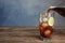 Pouring refreshing soda drink into glass with ice cubes and lime on wooden table against blue background