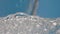 Pouring soda water into a glass on a blue background close up. Water fills a transparent glass, creating waves and air