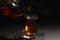 Pouring traditional Turkish tea from pot into glass on black table