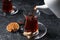 Pouring traditional Turkish tea from pot into glass on grey textured table, closeup