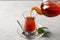 Pouring traditional Turkish tea from pot into glass on light grey table