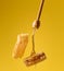 Pouring transparent sweet honey from a wooden stick on a wax honeycomb. Yellow background. Food levitates