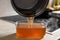 Pouring used cooking oil from saucepan into container on kitchen counter, closeup