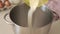 Pouring wheat flour from a measuring jug into a stainless steel bowl to prepare dough for baking