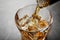 Pouring whiskey from bottle into glass with ice cubes on table