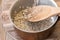 Pouring whole grain brown rice into copper pot on wooden spoon