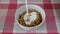 Pouring yogurt in bowl of whole grain muesli on a table with a red and white tablecloth