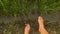 POV of dangling feet above green young paddy sporuts and mud on a beautiful peaceful rice field in the countryside