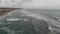 Pov flight over rough backwash sea  with foamy waves crashing on the shore and village skyline