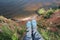 POV person feet in sneackers hanging from high send coast over lake or sea. Top view woman legs dangling over water. Personal