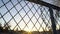 POV of person looking at amusement park through net fence, sunset on horizon