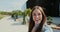 POV video call portrait of a young woman waving hand in casual clothes talking to friends while standing on city street.