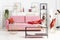 Powder pink couch with red pillow and blanket in apartment full of art and shelves