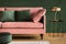 Powder pink sofa and golden lamp in a dark green living room interior. Real photo