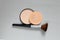 powder in a plastic round package and a brush on a gray background, women's cosmetics close up, foundation powder