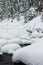 Powder snowdrifts on the stones of mountain river and forest snowfall