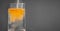 Powdered orange drink mix being poured into a clear glass of water