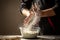 Powdery flour flying into air as man in black chef outfit wipes off his hands over table covered in flour. White flour flying into