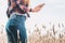 Power bank in the back pocket of a girl in a yellow field charges the phone, against the background of ears of wheat and sky, side